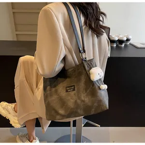 Detail of grey tote bag with black leather handles and plush charm on a model