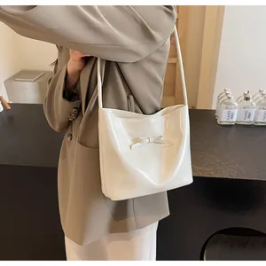 Detail showing creamy white glossy shoulder bag with elegant bow accent on model