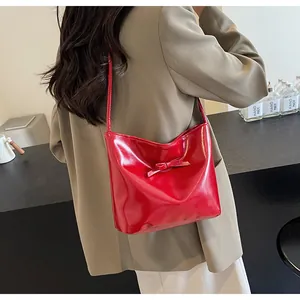 Detailed view of red glossy bucket bag with bow ornament on beige blazer model