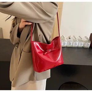 Macro detail of red glossy bucket bag featuring a decorative bow and slender strap