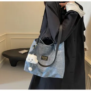 Detail of blue denim tote bag with black leather straps and white cloud plush charm