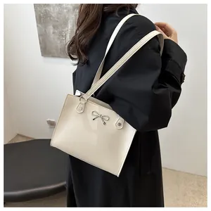 Close-up of cream shoulder bag with silver bow buckle on black coat background