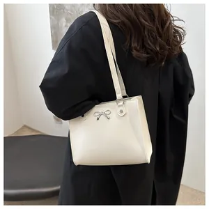 Detailed view of cream-white tote bag with silver bow buckle and rivet accents