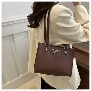 Detail view of a brown tote bag with silver bow ornament on a beige corduroy blazer