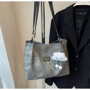 Detail of grey textured tote bag with black handles and white plush charm on a hanger