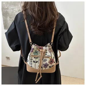 Detail view of a vintage floral bucket bag with leather base and drawstring on a model