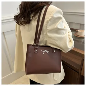 Detail of dark brown leather tote bag featuring a silver metal bow accent and rivet studs