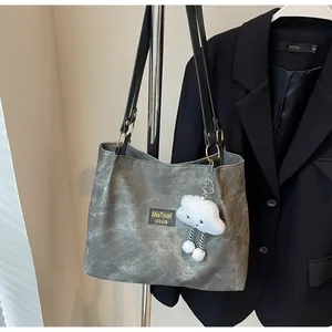 Detail of grey leather tote bag with square brand label and cloud plush pendant accessory