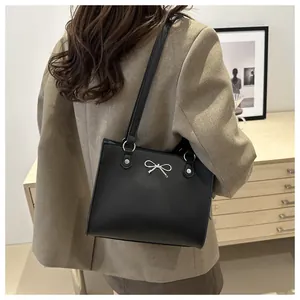 Detail of silver bow decoration and matte leather texture on large black tote bag