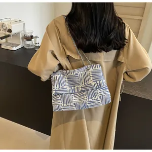 Detail of blue and white knit shoulder bag with silver chain strap on model in trench coat