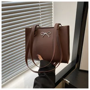 Close-up of a large dark brown tote bag with a silver metal bow detail and dual straps