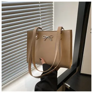 Detailed view of women's tote bag featuring a silver metal bow buckle on beige faux leather