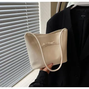 Detail view of a cream leather bucket bag featuring a minimalist bow and slim shoulder strap