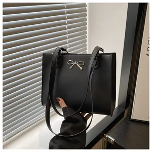 Close-up of black tote bag featuring a metallic silver bow and minimalist leather texture
