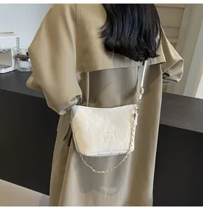 Détail du sac nuage plissé blanc avec chaîne dorée porté sur un trench-coat de couleur kaki