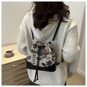 Detail of floral embroidery on ivory drawstring bucket bag with leather base