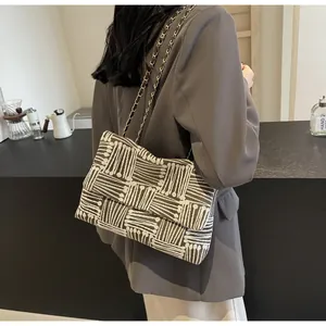 Detail of black and white striped woven crossbody bag with metal chain strap worn by a model