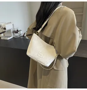 Détail d'un sac seau beige à texture marbrée avec chaîne en métal et écusson en cuir