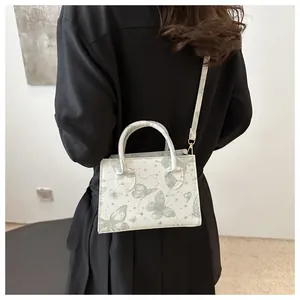 Close-up of white crossbody bag featuring green butterfly patterns and gold hardware