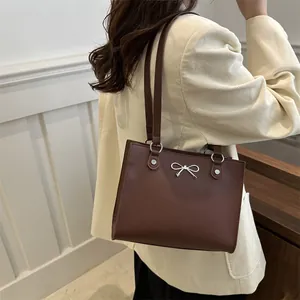 Brown leather large tote bag with silver bow charm on a beige corduroy jacket