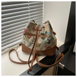 Detail of drawstring bucket bag featuring floral jacquard fabric and brown leather base