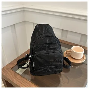Close-up of black textured crossbody bag with triple zippers on a wooden table