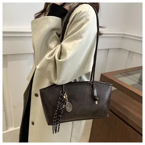 Dettaglio borsa tote marrone scuro con logo moda, ciondolo dorato e nappa intrecciata