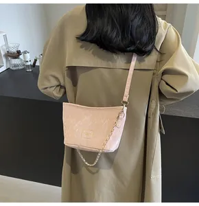 Détail du sac seau plissé rose clair avec chaîne dorée sur un trench-coat kaki chic