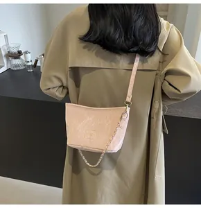 Détail du sac bandoulière en cuir froissé rose clair avec chaîne dorée porté par un mannequin