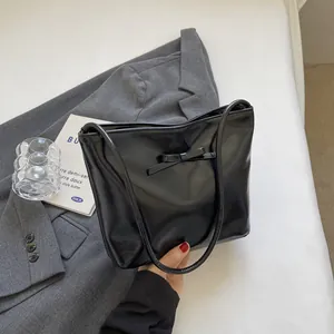 Minimalist black glossy bucket bag for women featuring a chic bow and slender strap