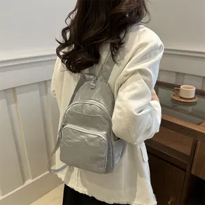 Silver-grey wrinkled nylon sling bag with adjustable strap shown on model in modern room