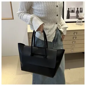 Minimalist black leather tote bag with cylindrical handles shown in a lifestyle setting