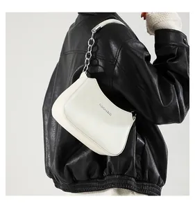 Primer plano de un bolso de hombro blanco de media luna con cadena sobre chaqueta cuero