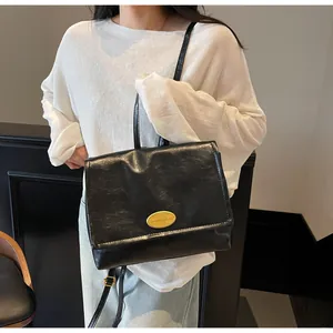 Detail of black textured leather bag with oval gold branding and adjustable shoulder strap