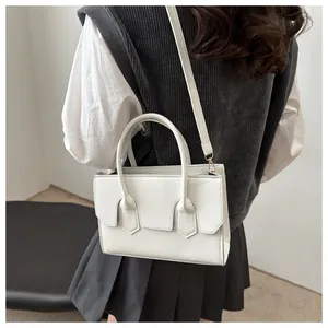 White structured rectangular handbag with gold hardware worn as a crossbody bag