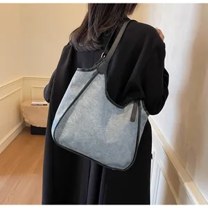Détail d'un grand sac cabas en denim avec finitions en cuir noir et bandoulière portee
