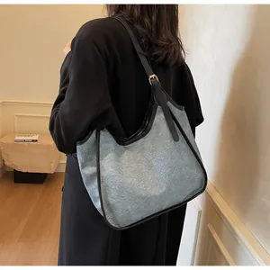 Détail du grand sac cabas en denim gris avec anses en cuir noir et boucles dorées