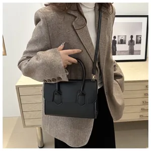 Detail of minimalist black leather shoulder bag with sleek handle and stitching on blazer