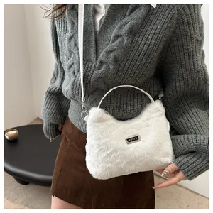 Detailansicht der weißen Kunstfell-Umhängetasche mit Sport-Plakette auf Strickpullover