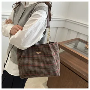 Detail der rot-braun karierten Tragetasche mit Leder-Markenlabel und goldener Kette