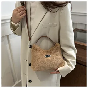 Detailaufnahme der khakifarbenen Plüschtasche mit sportlichem Metallemblem und Riemen