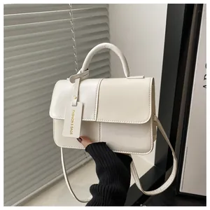 Detail einer cremeweißen Handtasche aus strukturiertem Kunstleder mit dezentem Logoanhänger