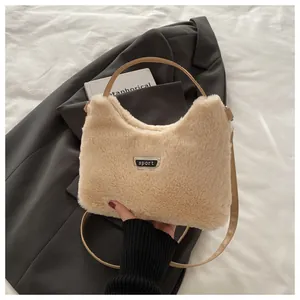 Detailstruktur der beigen Plüschtasche mit Metall-Sport-Logo auf grauem Stoff