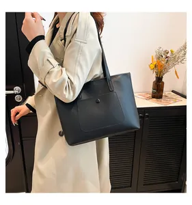 Détail du sac cabas minimaliste en cuir PU noir porté par un mannequin en trench-coat