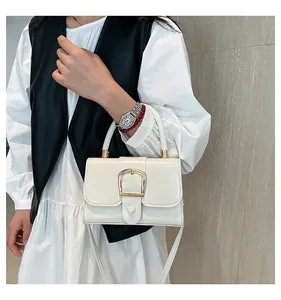 Dettaglio di una borsa a tracolla chic in pelle crema con fibbia dorata su una modella