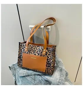 Detail of leopard print tote bag with brown leather handles on a blue denim jacket