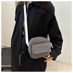 Detail of grey canvas crossbody bag with red heart pattern and white textile strap