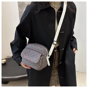 Detail of grey canvas crossbody bag with red heart patterns and wide white strap