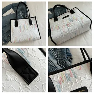 Detail of white quilted tote bag with colorful wavy stitching and black leather handles