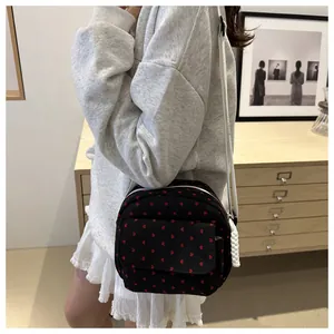 Close-up of black crossbody bag with red heart pattern and adjustable white strap